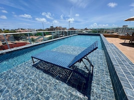Una piscina en la azotea con barandilla de vidrio, una tumbona y vistas panorámicas de la ciudad.