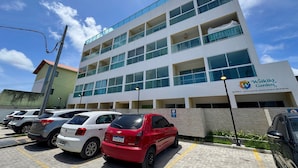 A multi-story building with a sign for Waikiki Garden, a parking lot with several cars, and a clear blue sky. - Waikiki Garden (Ipojuca)