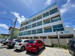 A multi-story building with a sign for Waikiki Garden, a parking lot with several cars, and a clear blue sky. - Waikiki Garden (Ipojuca)