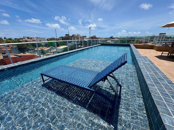 A rooftop swimming pool with a glass barrier, a lounge chair, and a view of the cityscape. - Waikiki Garden (Ipojuca)