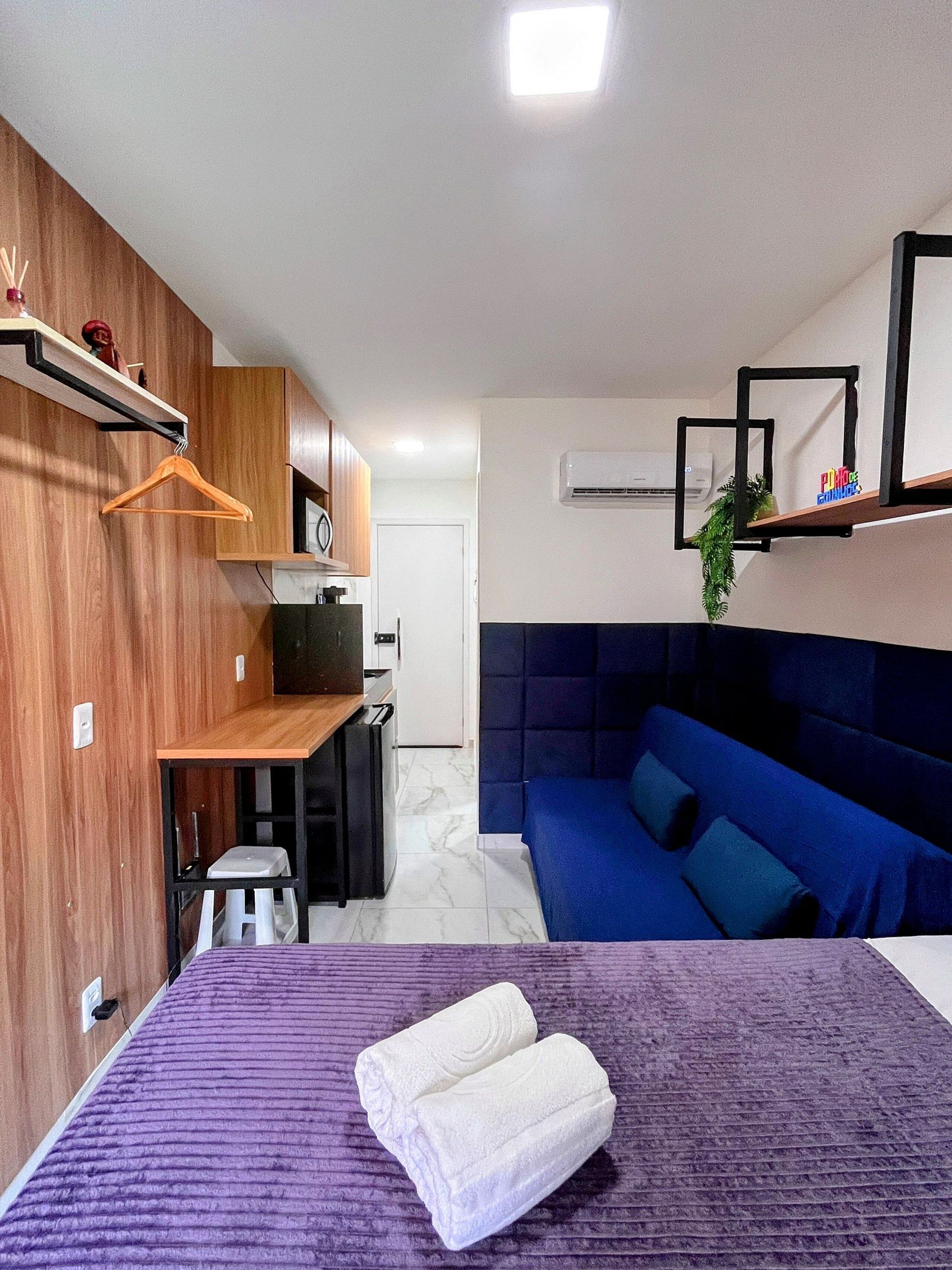 A compact room with a bed, a small kitchenette, a blue sofa, and a wooden wall.