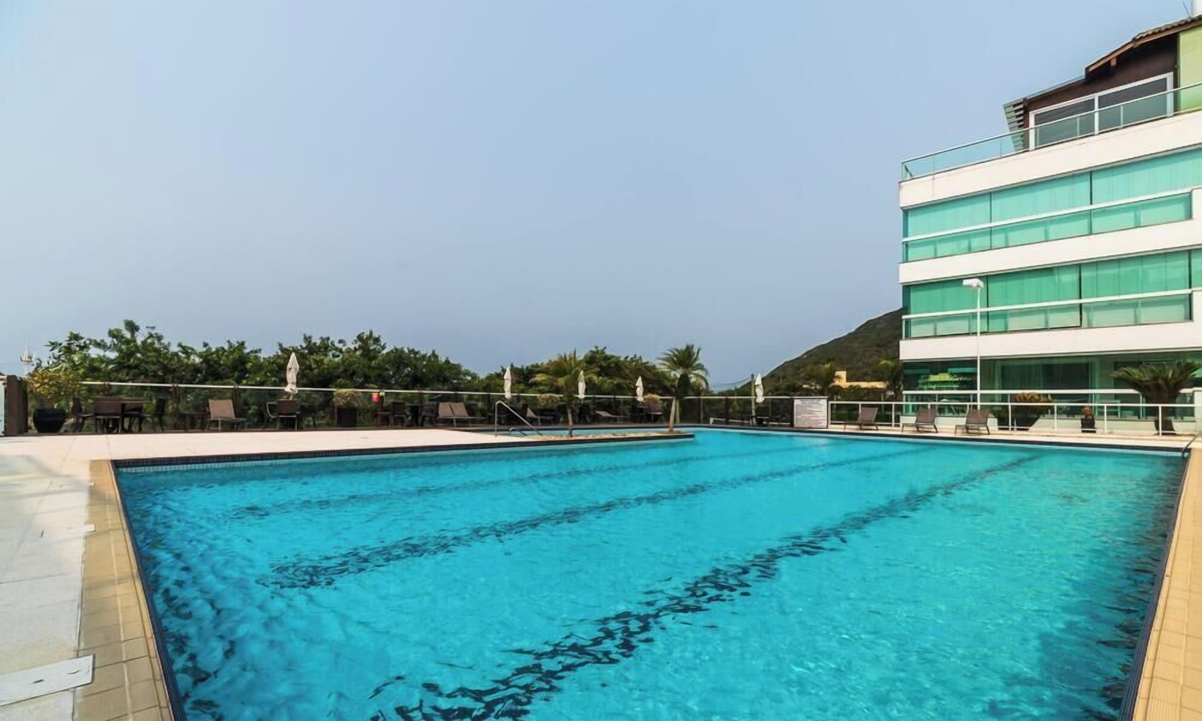 Une piscine à l’eau d’un bleu cristallin, entourée de chaises longues et de parasols, avec un bâtiment moderne en arrière-plan.