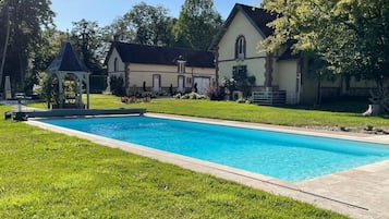 Een zwembad met een prieel en een huis op de achtergrond.