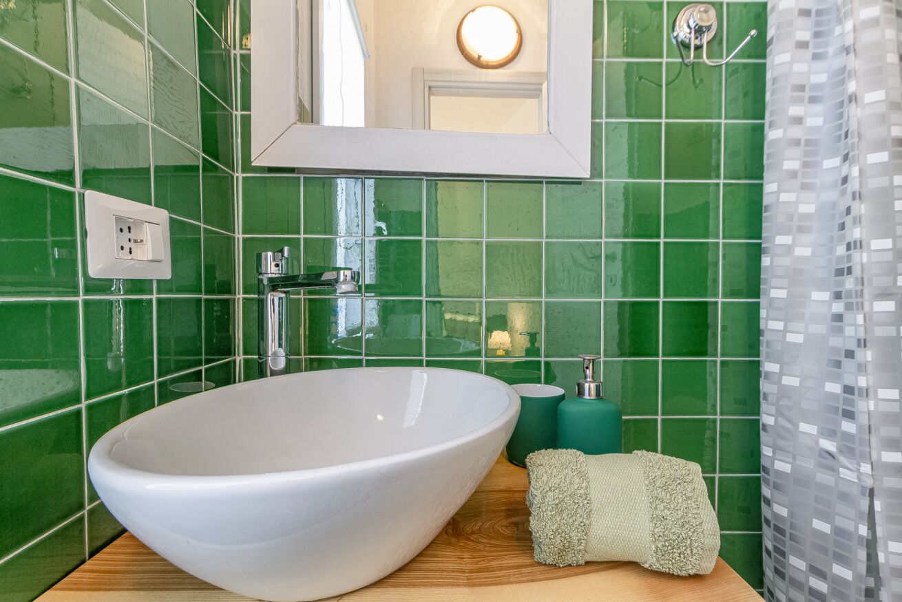 Un baño con un lavamanos grande blanco, paredes de azulejos verdes, un espejo y una cortina de ducha.