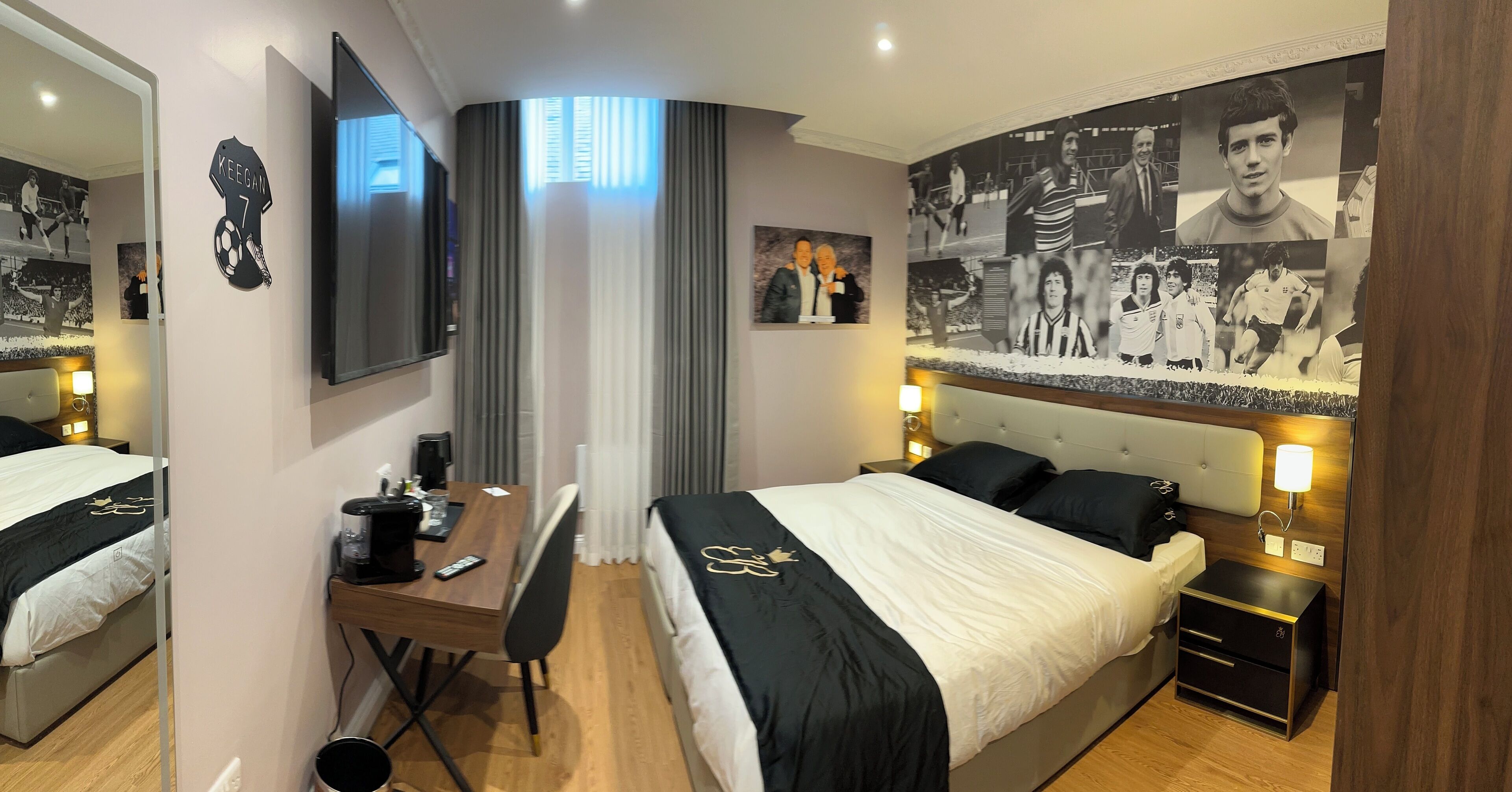 A hotel room with a bed, desk, chair, and a large wall mural.