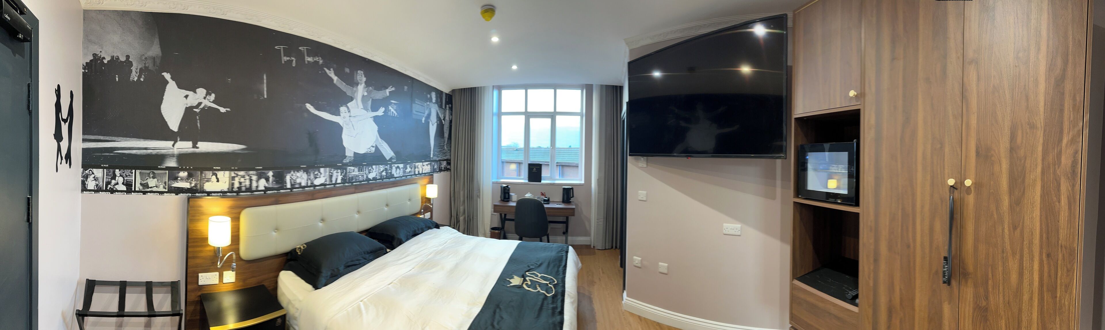 A hotel room with a large bed, a desk with a chair, a television, and a wardrobe.
