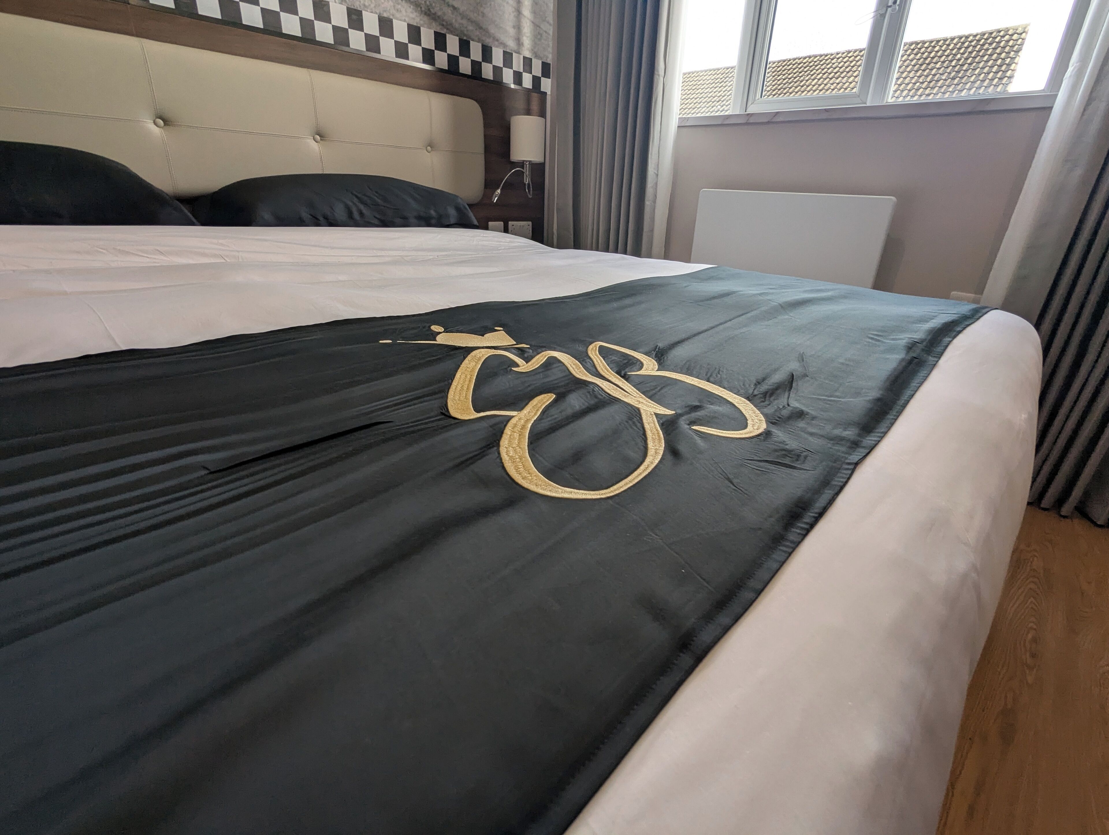 A bed with a black and white bedspread, a headboard with a checkered pattern, and a window with curtains.