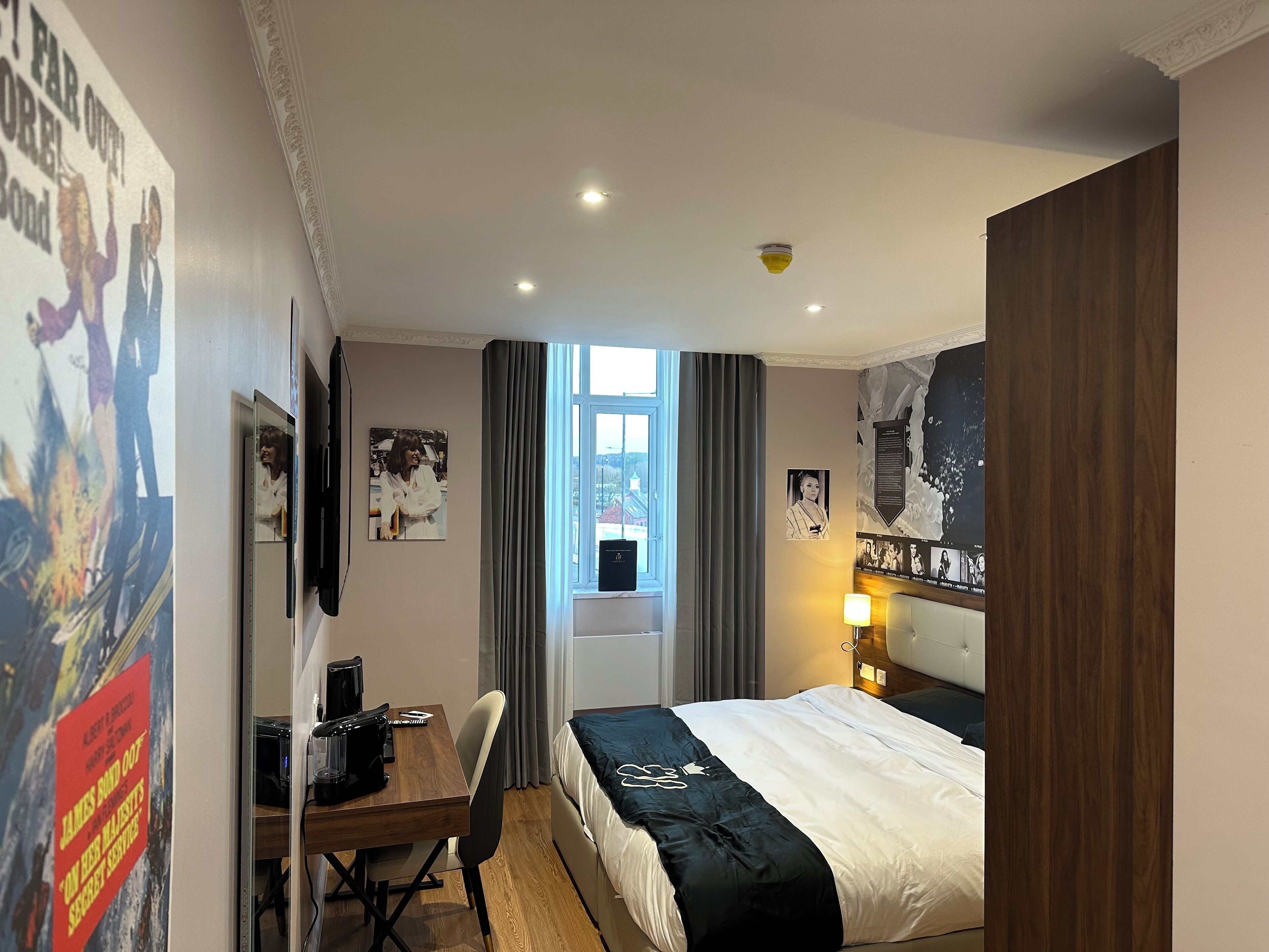 Een hotelkamer met een bed, een bureau, een stoel, een raam met gordijnen en decoratie aan de muur.