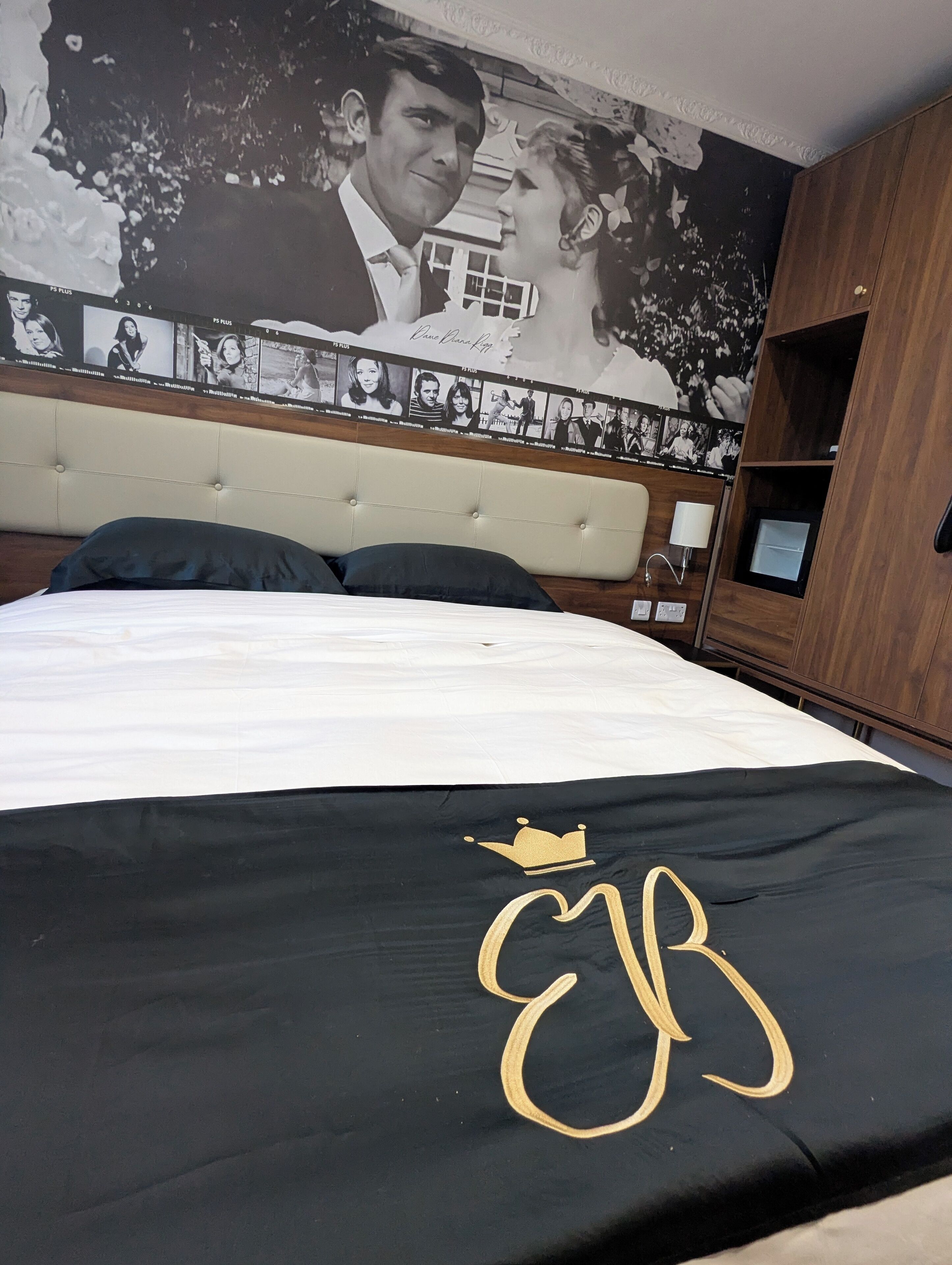 Una camera da letto con un letto, una testiera con collage fotografico, un cuscino decorativo nero e dorato e un armadio in legno.