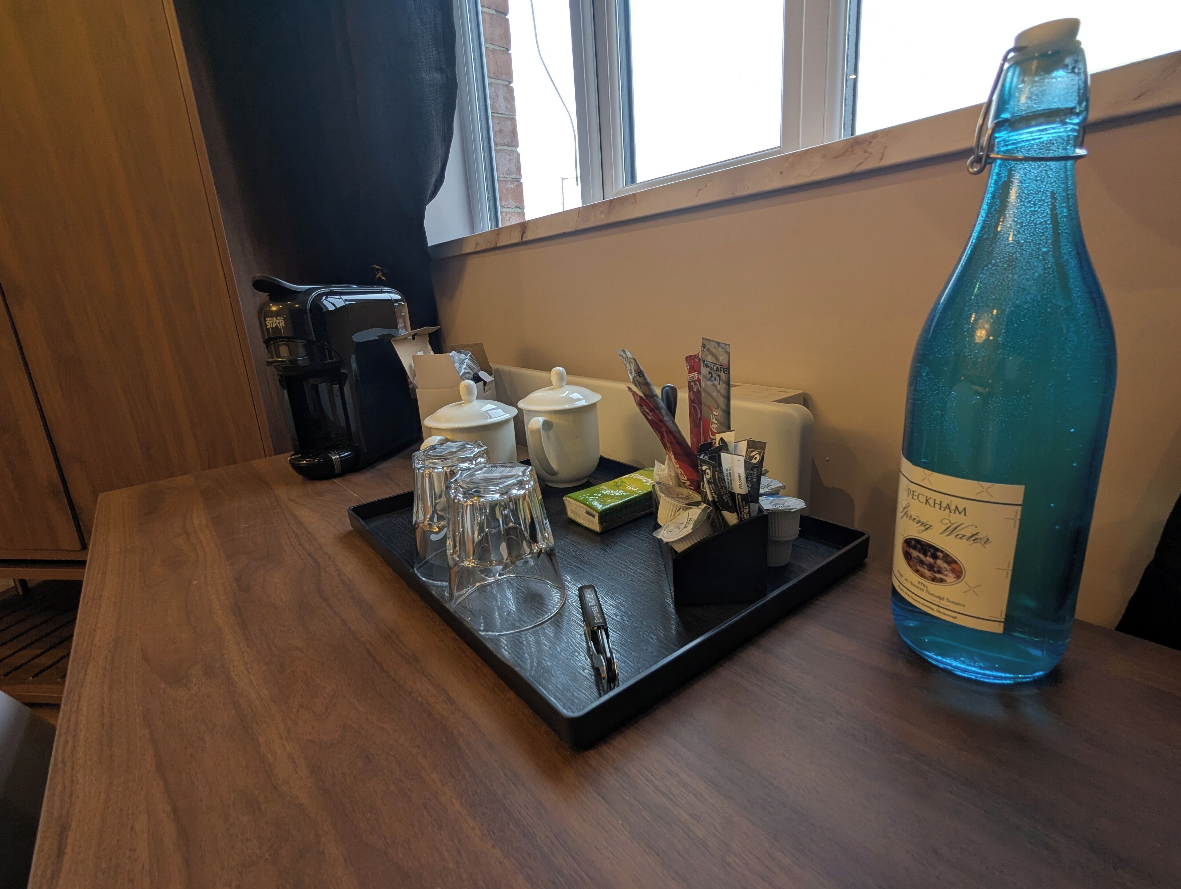 Ein Holztisch mit einer Tablett, das eine Wasserflasche, Gläser und eine Kaffeemaschine trägt.