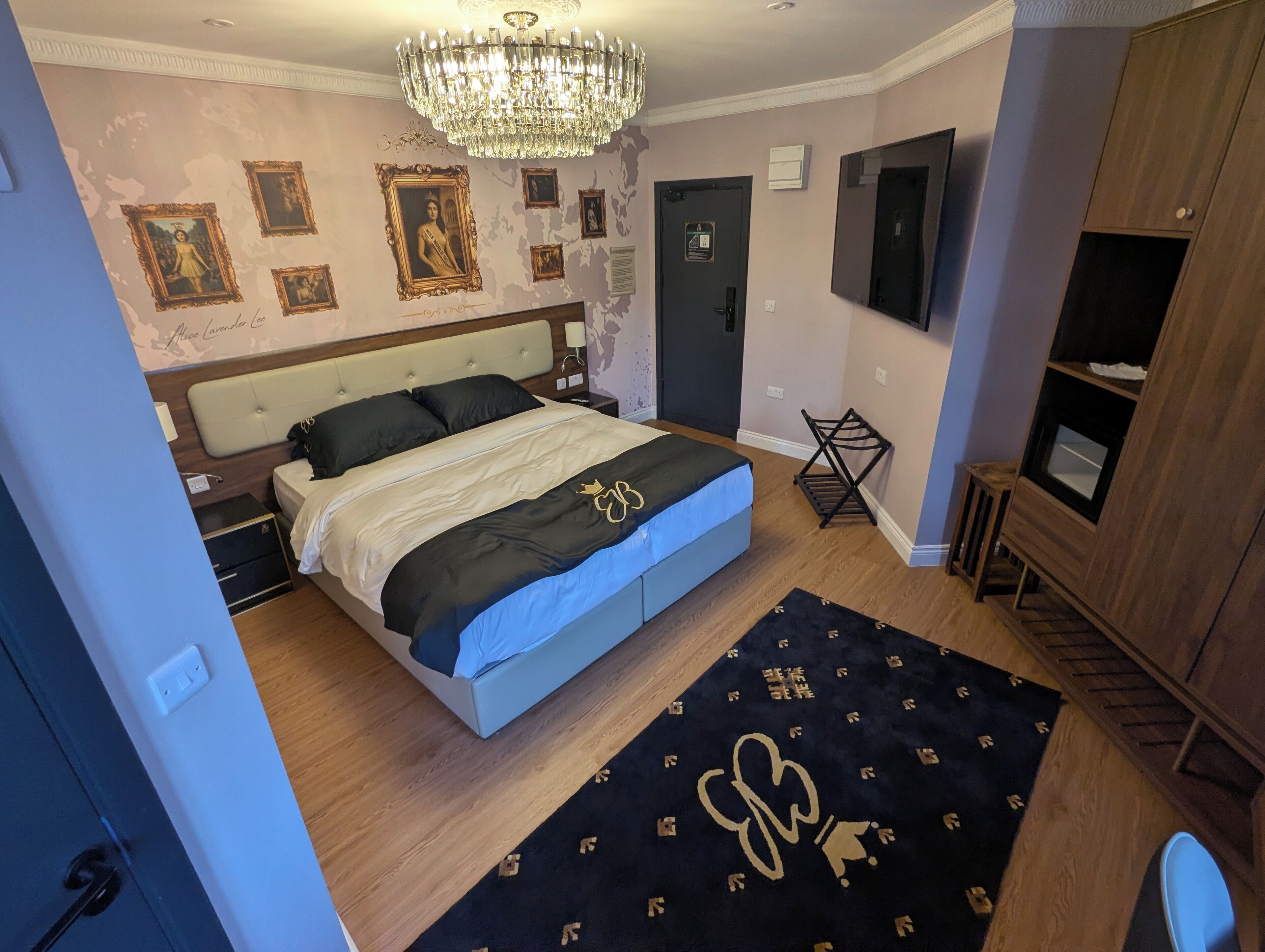 A bedroom with a large bed, a chandelier, a wardrobe, and a TV.