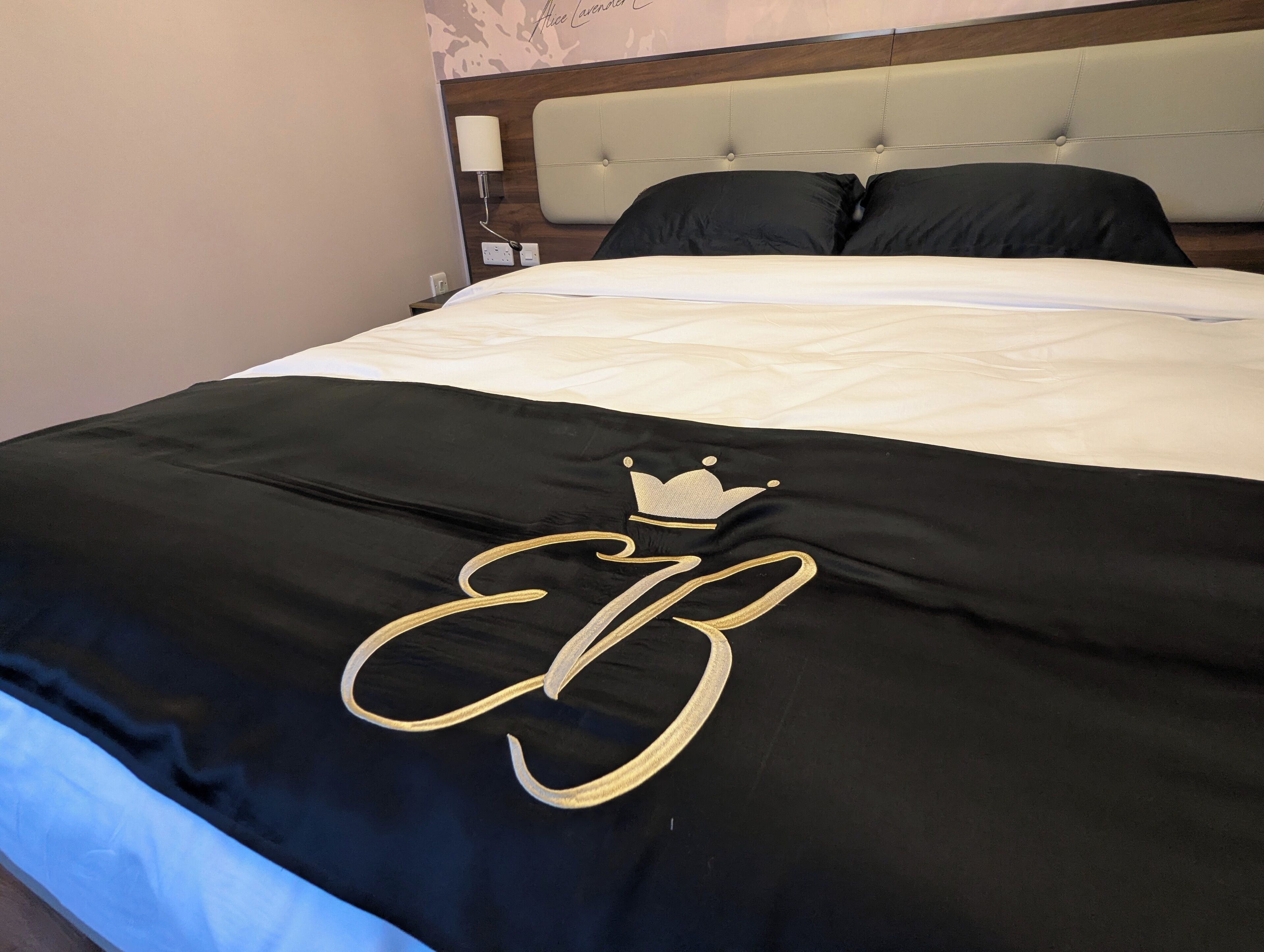 Una cama con colcha blanco y negro que presenta un bordado con una corona y las letras 'EB'.