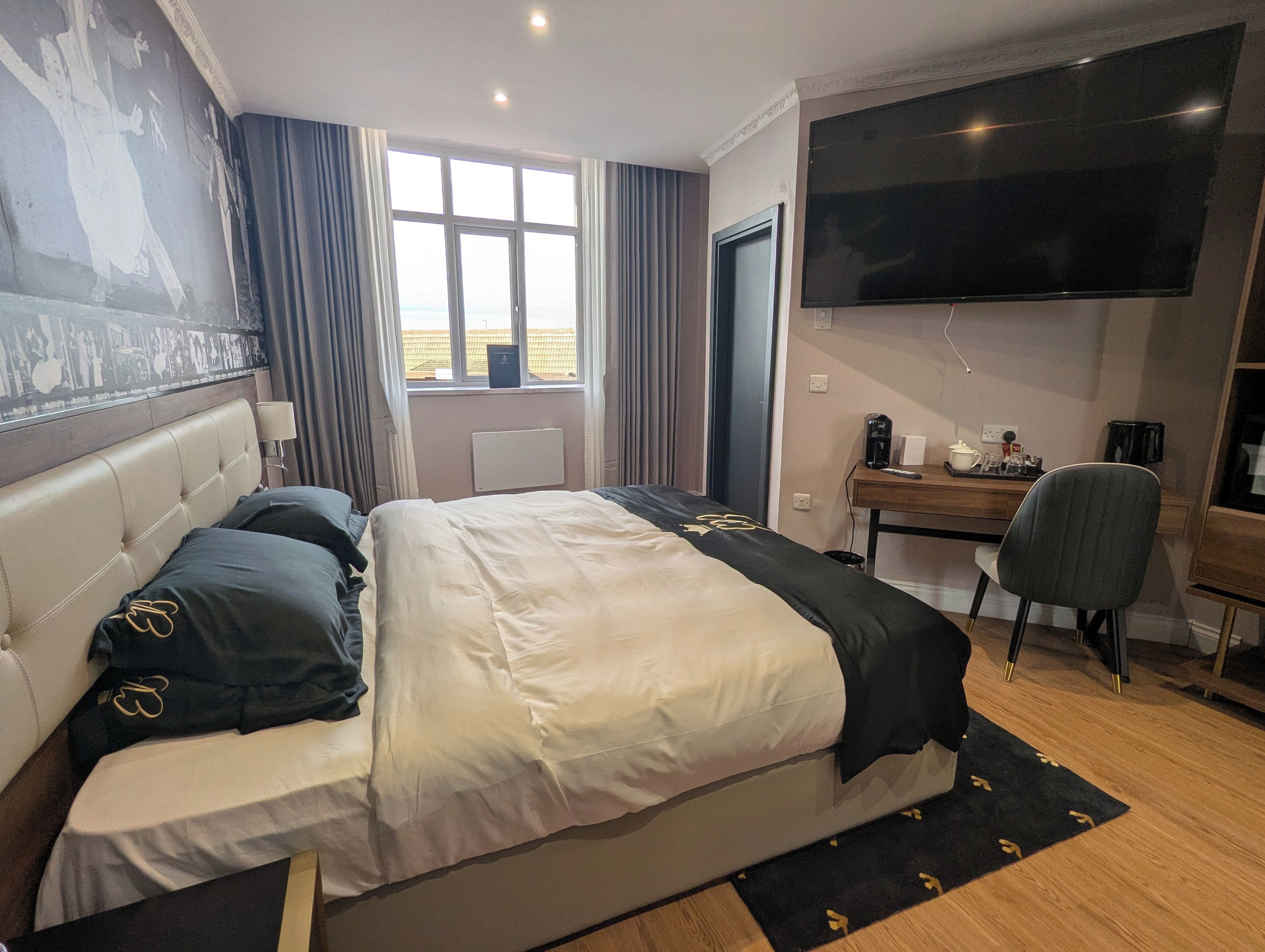 A hotel room with a large bed, a desk with a chair, a flat-screen TV, and a window with curtains.