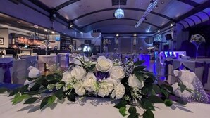 A banquet hall with tables set for a formal event, featuring floral centerpieces and a bar area in the background. - Empress Building (Mexborough)