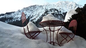 Ein mit Schnee bedeckter Außenbereich mit Metallstühlen und einem Tisch, vor einer Berglandschaft.