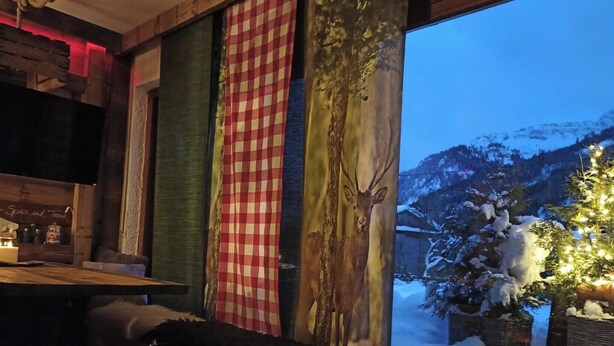 Ein Zimmer mit großem Fenster, Holzwand und Blick auf schneebedeckte Berge.