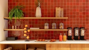 A kitchen with red tiles, wooden shelves, a plant, and various kitchen items. - Hotel Middelland Rotterdam (Rotterdam)