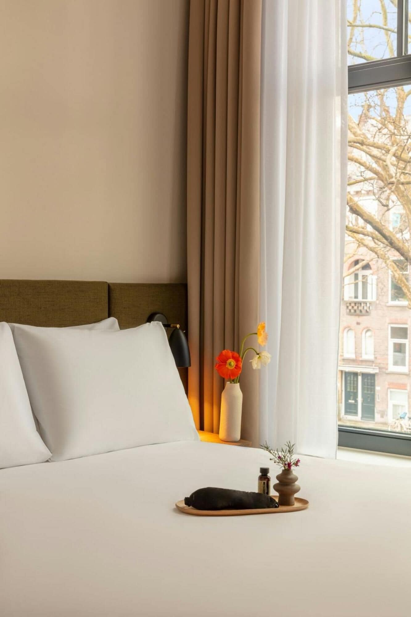 A neatly made bed with white linens, a dark headboard, and a window with curtains.