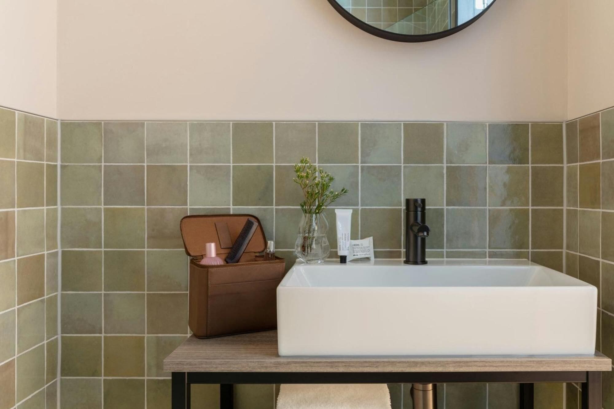 Un baño con un lavamanos rectangular, un espejo encima y una pared con azulejos.