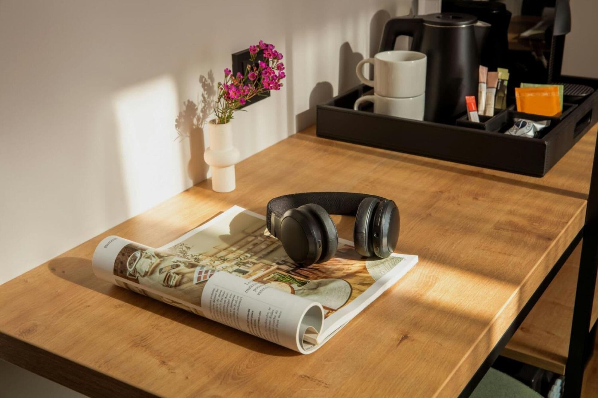 Une table en bois sur laquelle se trouvent un magazine enroulé, une paire d’écouteurs, une machine à café, une tasse et un plateau avec des capsules de café et un petit objet orange.