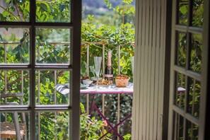 Une vue à travers une fenêtre sur une table dressée, avec une bouteille, des verres et un bol, le tout entouré d'une végétation luxuriante.