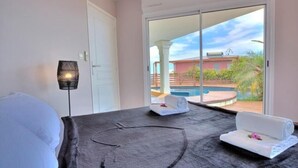 Ein Hotelzimmer mit Bett, Massagetisch, Handtuch und Blick auf Pool und Außenbereich.