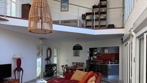 Ein großzügiger Wohnbereich mit einem roten Sofa, einem Holztisch und einem Fernseher. Im Hintergrund ist ein Essbereich mit einer Küche erkennbar.