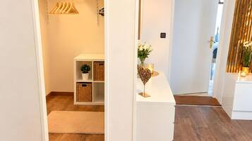 A hallway with a white console table, a potted plant, and a candle. There is a wooden floor and a door leading to another room.
