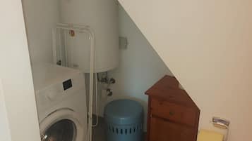 Ein Waschbereich mit einer Waschmaschine, einem blauen Mülleimer und einem Holzschrank.