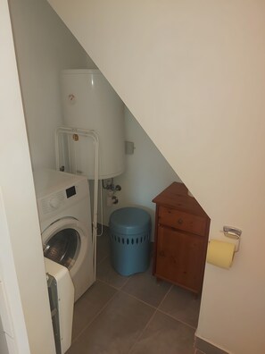 A laundry area with a washing machine, a blue trash bin, and a wooden cabinet. - Apartment 'Golden Base' with Mountain View, Wi-Fi and Air Conditioning (Villach)