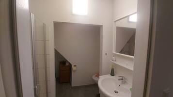 Casa de banho com lavatório branco, espelho e pequeno armário.