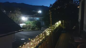 A balcony with a view of a street and mountains, decorated with string lights and ivy.