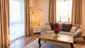 A modern living room with a sofa, a coffee table with a vase of flowers, a standing lamp, and sheer curtains.