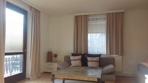 A living room with a sofa, a coffee table, a side table, and a window with curtains. - Apartment 'Golden Base' with Mountain View, Wi-Fi and Air Conditioning (Villach)