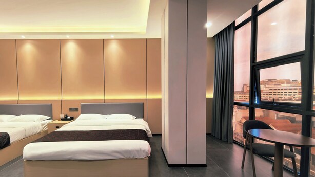 Une chambre d’hôtel moderne, dotée d’un grand lit, d’un bureau et offrant une vue sur la ville grâce à de larges fenêtres.