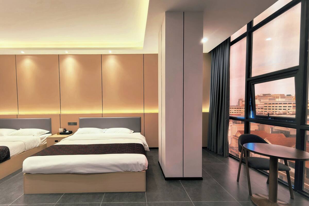 Una habitación de hotel moderna con una cama grande, un escritorio y vistas de la ciudad a través de amplios ventanales.