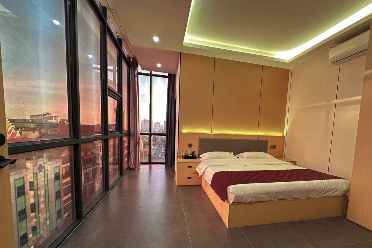 Un dormitorio moderno con una cama grande, una mesita de noche y un armario. Una ventana grande ofrece vistas de edificios exteriores.