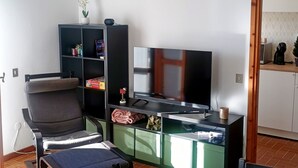 Ein Wohnzimmer mit Fernseher, einem Sessel, einem Bücherregal und einem kleinen Tisch mit einer Tasse.