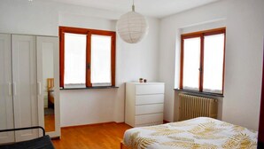 Ein Schlafzimmer mit einem Bett, einem Schminktisch, einem Heizkörper und zwei Fenstern mit Holzrahmen.