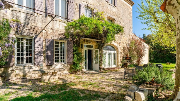 Um edifício de pedra com entrada para um jardim, uma pequena porta e uma janela com persianas.