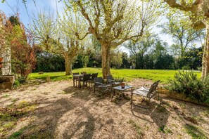 An outdoor seating area with tables and chairs, surrounded by trees and a grassy field. - Room 'Camille' Le Mas de Kitty, shared pool (Saint-Rémy-de-Provence)