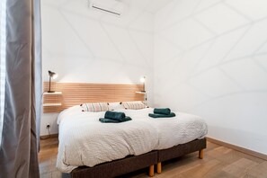 A bedroom with a bed, bedside lamps, a wooden headboard, and a wall-mounted air conditioner. - Room 'Camille' Le Mas de Kitty, shared pool (Saint-Rémy-de-Provence)