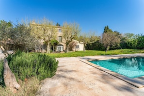 Un espace aménagé au bord de la piscine, avec une terrasse en pierre, une piscine et une grande maison dotée d’un jardin.