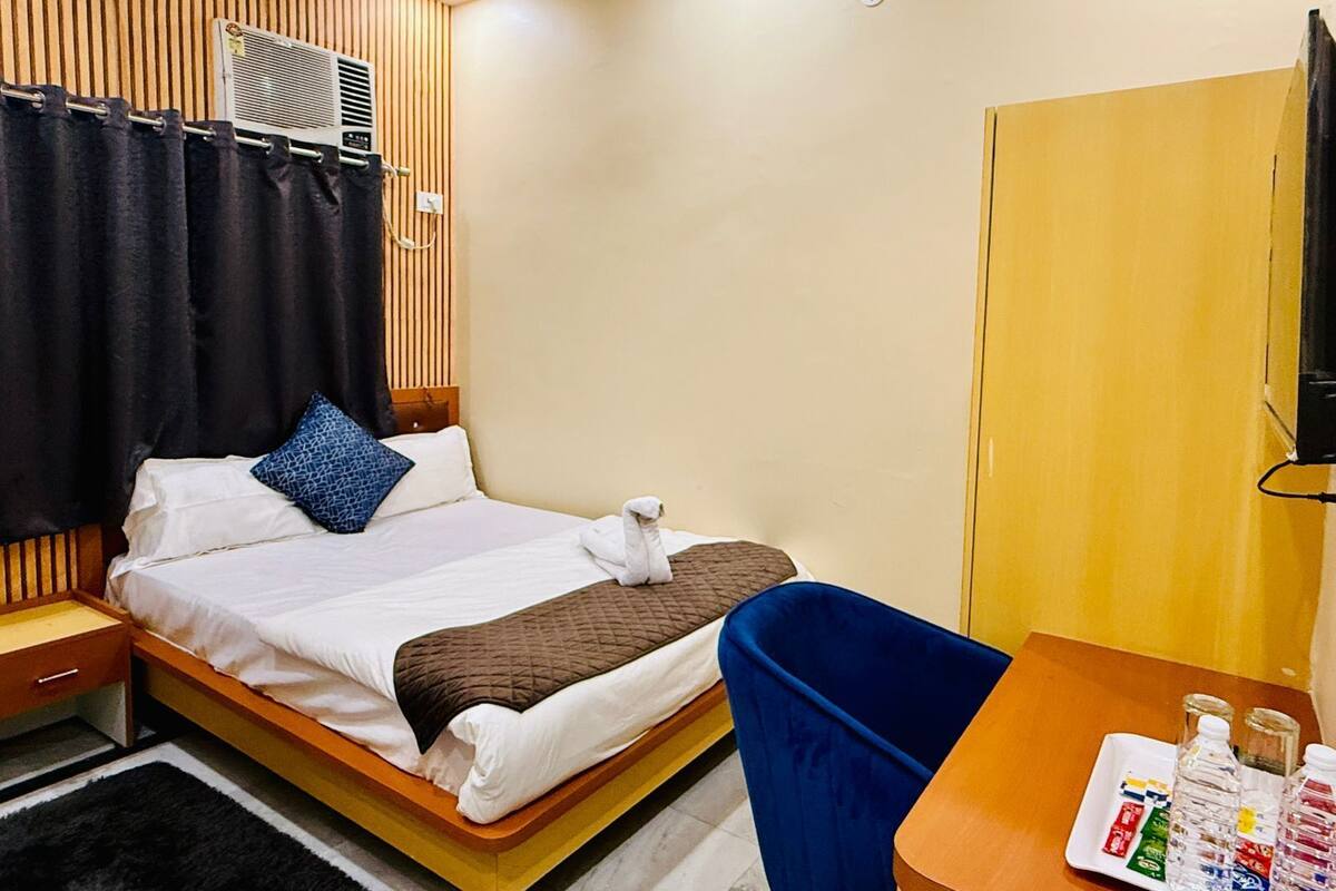 Ein Hotelzimmer mit Bett, Holz-Kopfteil, Schreibtisch mit Stuhl und kleinem Tisch mit Toilettenartikeln.