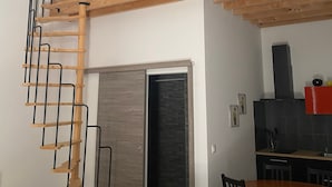 A modern kitchen with a wooden ceiling, a black hanging light fixture, and a dining area with a wooden table and chairs. - Spacious Studio Le Mas de Kitty, Shared Garden and Pool (Saint-Rémy-de-Provence)
