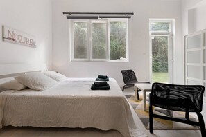 Une chambre à coucher avec un lit, une chaise, une table et une fenêtre donnant sur un paysage verdoyant.