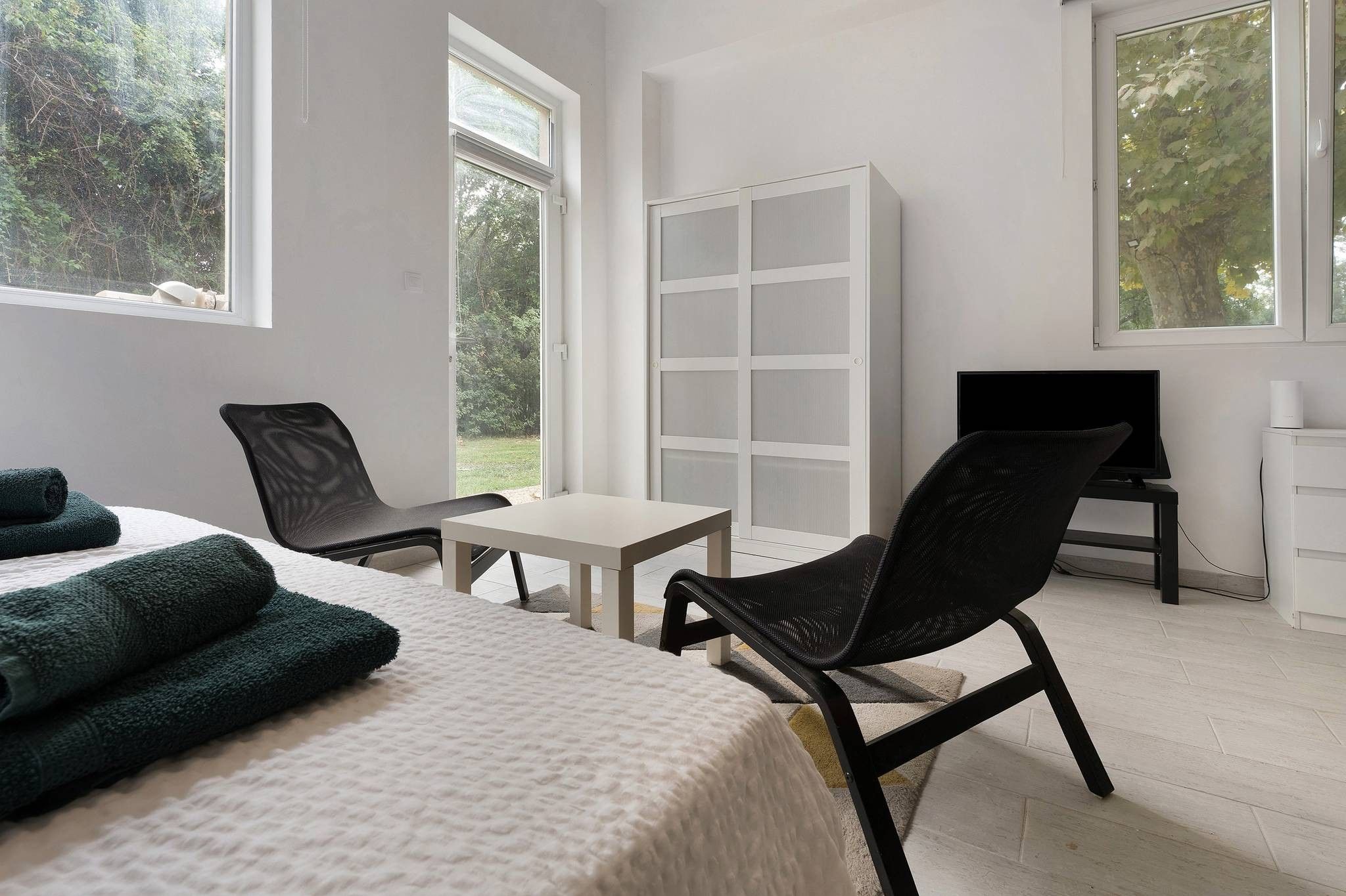 A hotel room with a bed, a chair, a small table, a TV, and a cabinet.