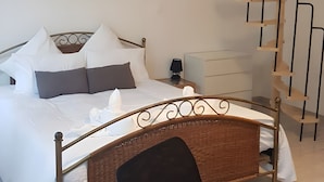 Ein Schlafzimmer mit einem Bett, einem Sessel, einem Nachttisch, einer Lampe, einem Wandbild und einer Holzspirale.