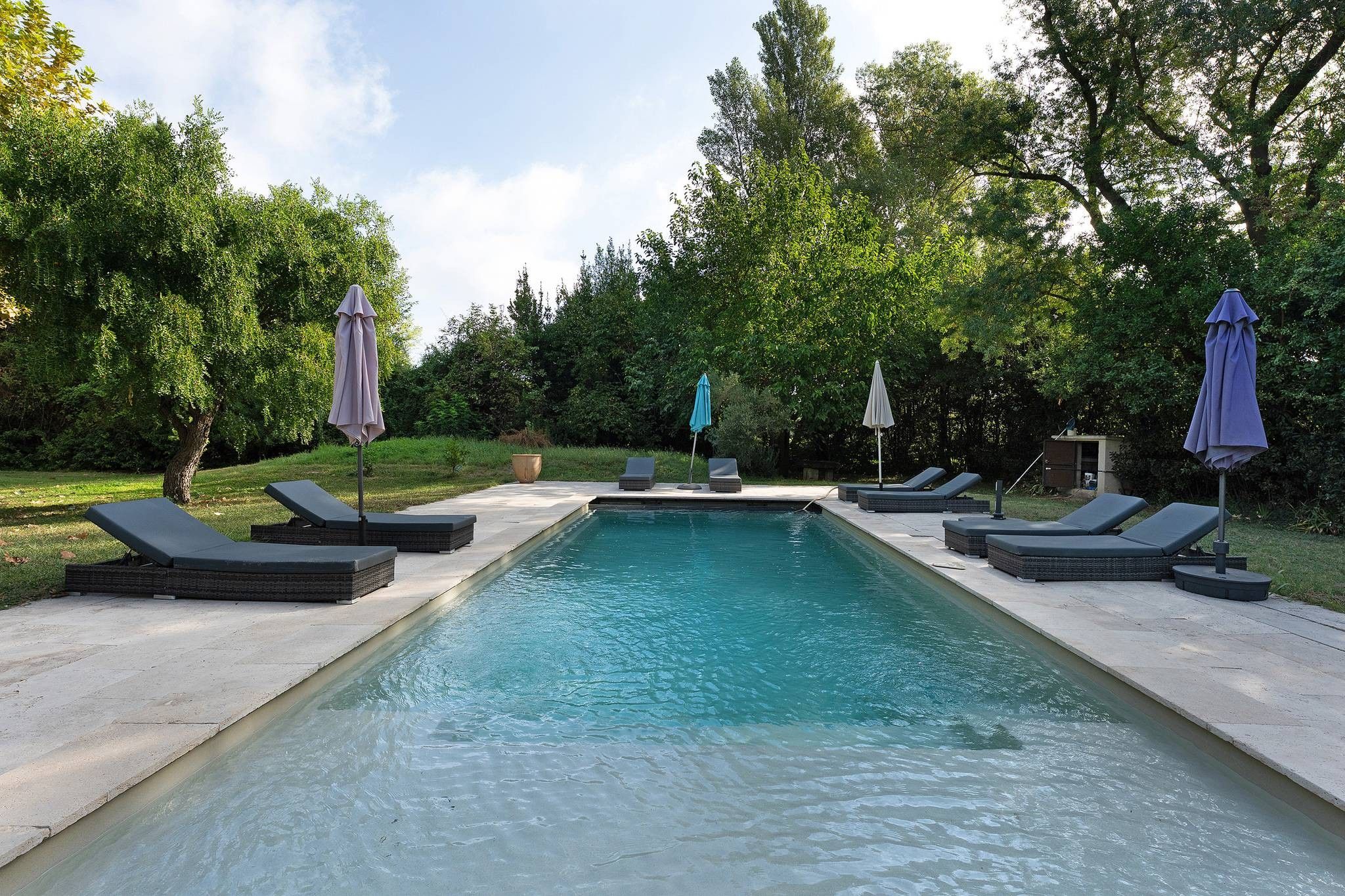 A rectangular swimming pool with lounge chairs and umbrellas.