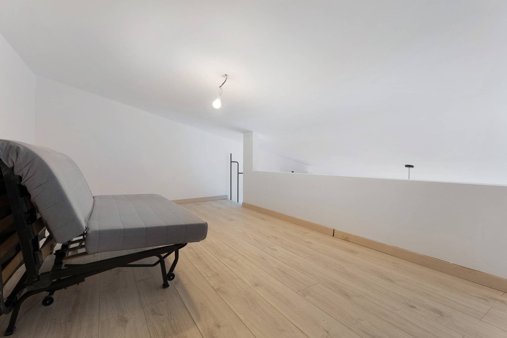 A room with a bed, a wooden floor, and a white ceiling.